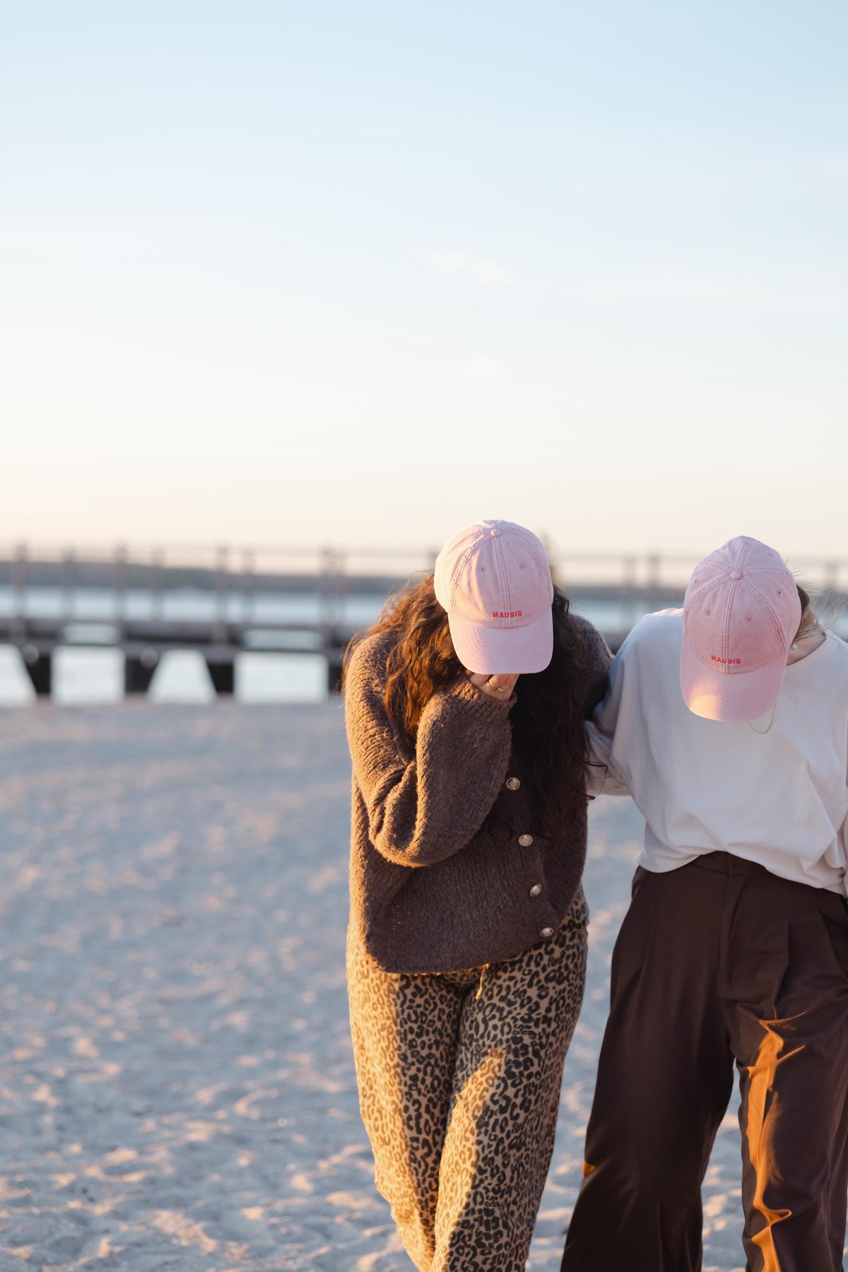 Zwei Personen mit rosa bestickten PAMULA Caps am Strand